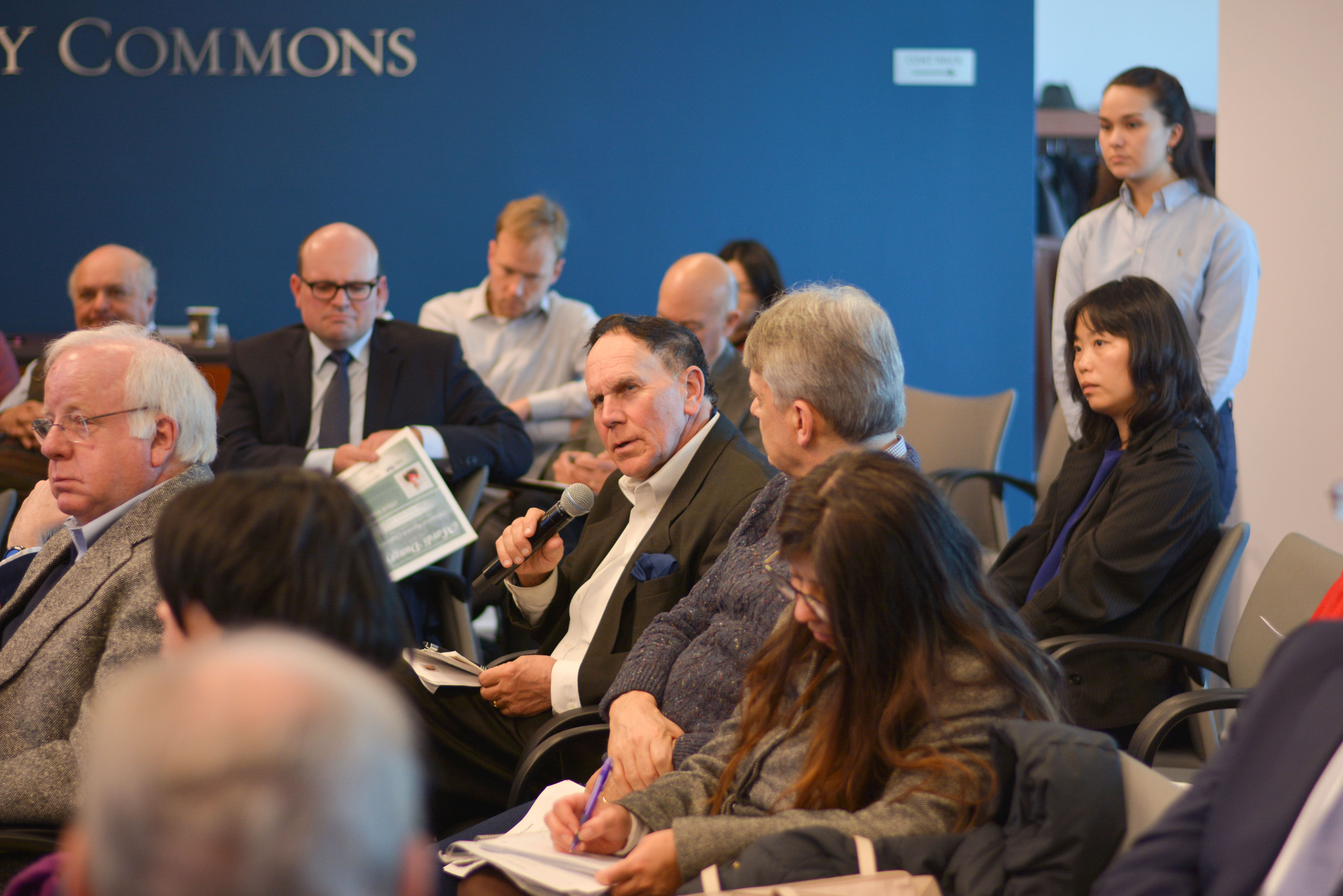 Audience members at an economics event listening as one person talks into a microphone