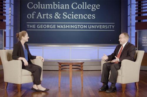 Tara Sinclair and Dean Paul Wahlbeck talking on a stage in front of a Columbian College of Arts and Sciences banner